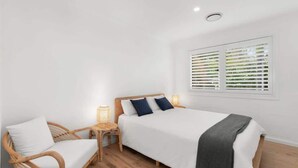 A bedroom with a bed, a chair, a nightstand, a window with blinds, and a ceiling light.