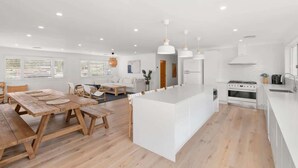 A modern kitchen with a central island, wooden dining table, and pendant lighting.