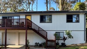 A two-story house with a balcony, a garage, and a small front yard with potted plants. - Coastal Chillout at Mossy (Mossy Point)