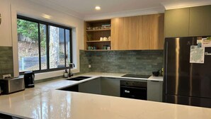 A modern kitchen with a large island, built-in appliances, and a window with a view of the outdoors. - Coastal Chillout at Mossy (Mossy Point)