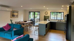 A modern kitchen with a dining area, a sofa, and a large window. - Coastal Chillout at Mossy (Mossy Point)