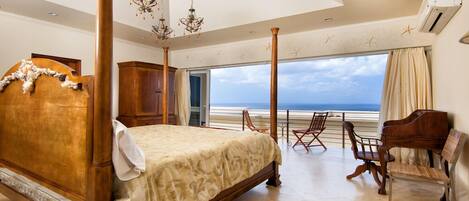 A bedroom with a large bed, a wooden wardrobe, a piano, and a view of the ocean.