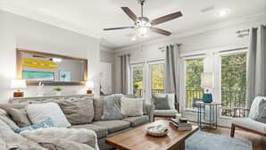 A modern living room with a ceiling fan, a large window with blinds, a sofa set, and a coffee table. - Beatles Retreat, 5 min WALK to Beach + Golf Cart & Arcade Machine, Dog Friendly! (Miramar Beach)