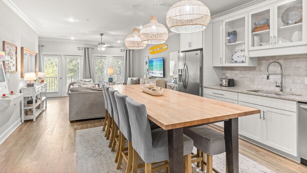 A modern kitchen with a wooden dining table, grey upholstered chairs, and pendant lighting. - Beatles Retreat, 5 min WALK to Beach + Golf Cart & Arcade Machine, Dog Friendly! (Miramar Beach)