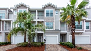 A multi-story residential building with a brick pathway leading to the entrance, surrounded by well-maintained landscaping and palm trees. - Beatles Retreat, 5 min WALK to Beach + Golf Cart & Arcade Machine, Dog Friendly! (Miramar Beach)