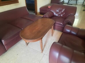 A living room with a brown wooden coffee table, a red leather sofa, and a matching armchair. - OYO Life 93160 Kost Jenny Karawang (Karawang)