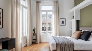 A bedroom with a bed, a desk, and a view of a building through a window. - ATH121 - Elysian 2BR Apartment in Plaka 1 (Athina)