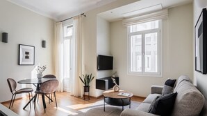A modern living room with a sofa, a coffee table, a TV, and a dining area with chairs and a table. - ATH121 - Elysian 2BR Apartment in Plaka 1 (Athina)