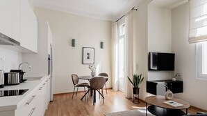 A modern kitchen with white cabinets, a dining area with a table and chairs, a flat-screen TV mounted on the wall, and a potted plant on the floor. - ATH121 - Elysian 2BR Apartment in Plaka 1 (Athina)