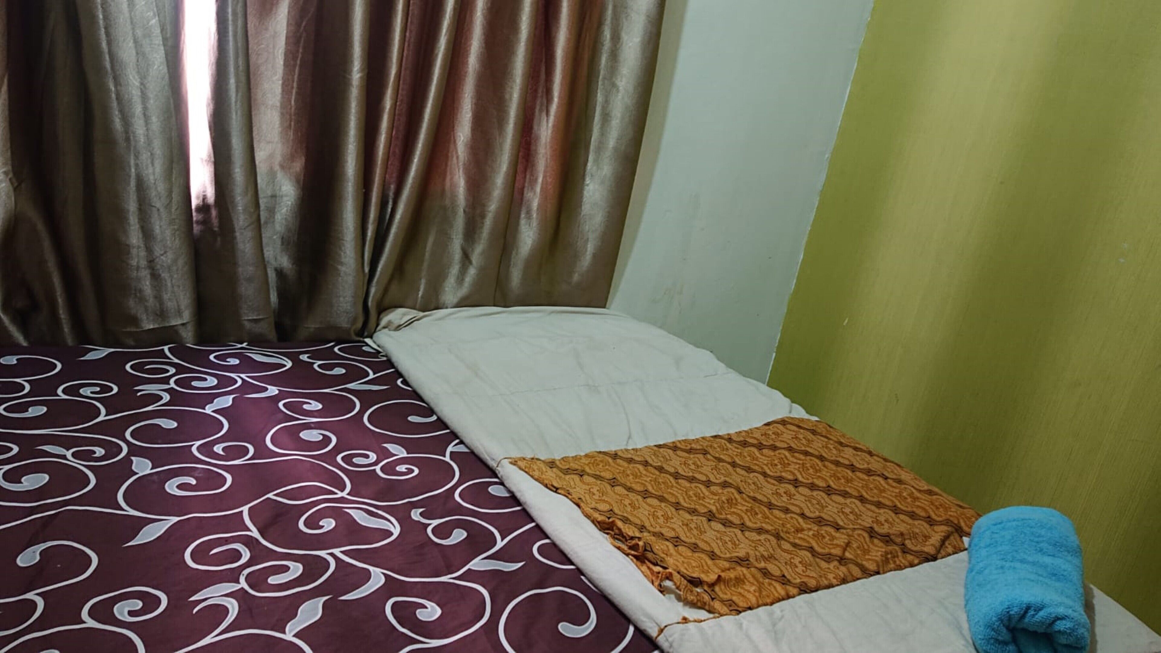 Un lit simple avec une couvre-lit à motifs, un plaid marron et une serviette bleue posée sur le côté.