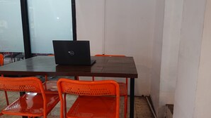 A conference room with a wooden table, a laptop, and orange chairs. - OYO Life 93139 Apartemen Grand Sentraland By Evi (Karawang)
