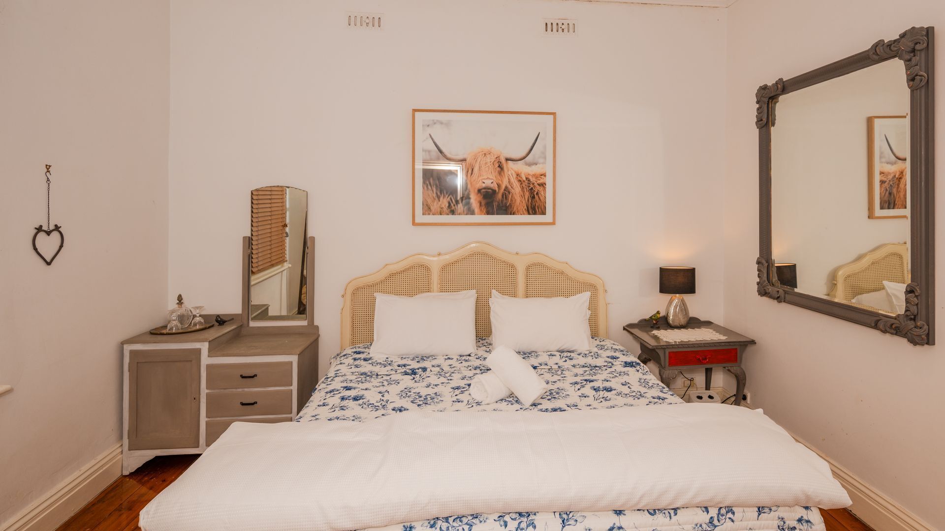 Une chambre à coucher avec un lit, une table de chevet, un miroir et un tableau encadré accroché au mur.