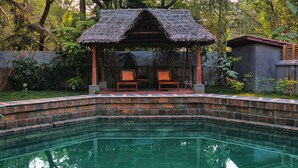 A pool with a brick edge, a thatched-roof gazebo, and two lounge chairs. - Chittoor Kottaram - CGH Earth (Kanayannur)