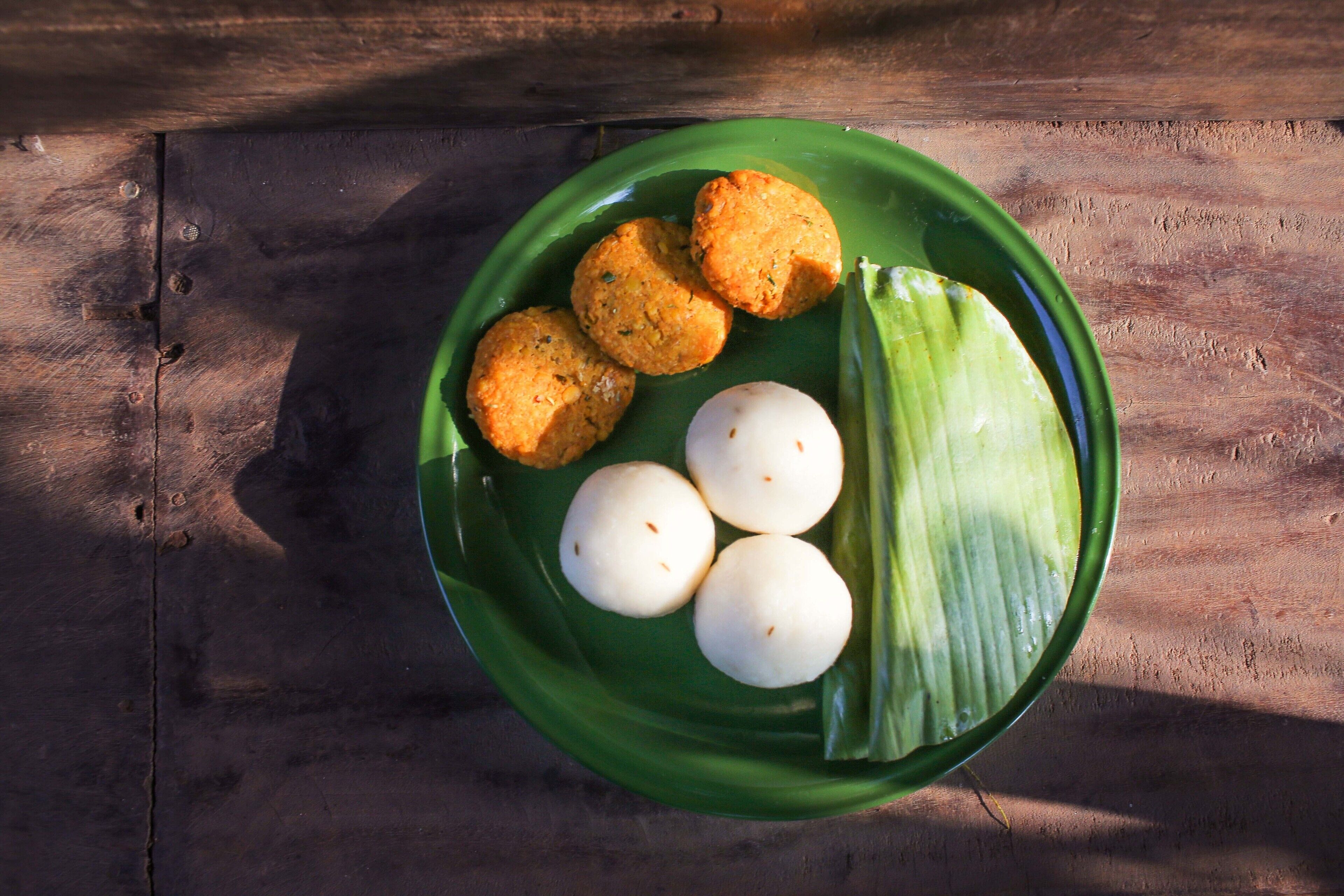 A green plate with three round, golden-brown items and two white round items on a wooden surface.