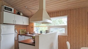 A compact kitchen with wooden walls, a white refrigerator, a microwave, a sink, and a small dining area with a chair. - "Fasti" - 300m from the sea by Interhome (Gilleleje)