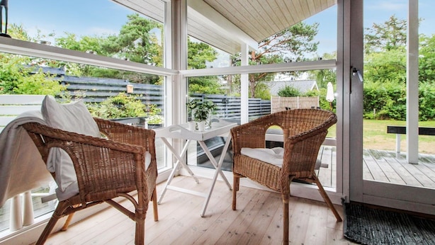 A covered patio area with wicker chairs and a table, large windows, and a view of a garden and house. - "Fasti" - 300m from the sea by Interhome (Gilleleje)