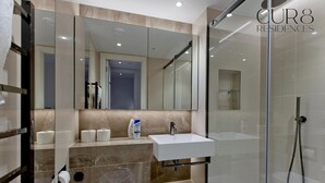 A modern bathroom with a glass shower enclosure, a white sink, and a marble-tiled vanity. - Modern Urban Retreat in Vibrant West London (London)