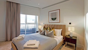 A hotel room with a large bed, a nightstand, a window with curtains, and a framed artwork on the wall. - Modern Urban Retreat in Vibrant West London (London)