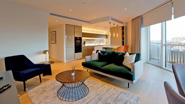 A modern living room with a sofa, a coffee table, and a TV. There is a kitchen area visible in the background. - Modern Urban Retreat in Vibrant West London (London)