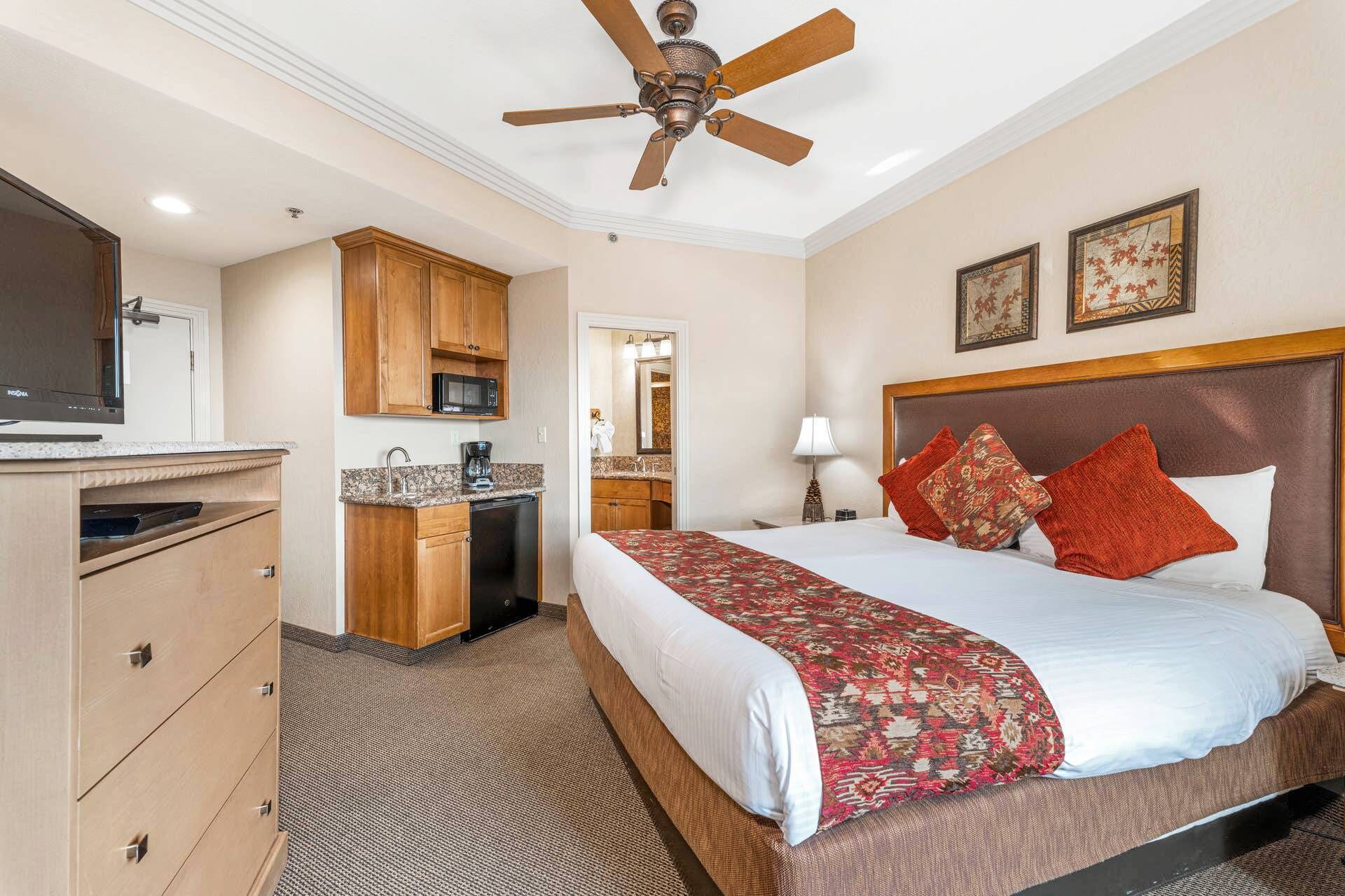 Une chambre d’hôtel équipée d’un lit, d’un bureau, d’une kitchenette et d’un ventilateur de plafond.