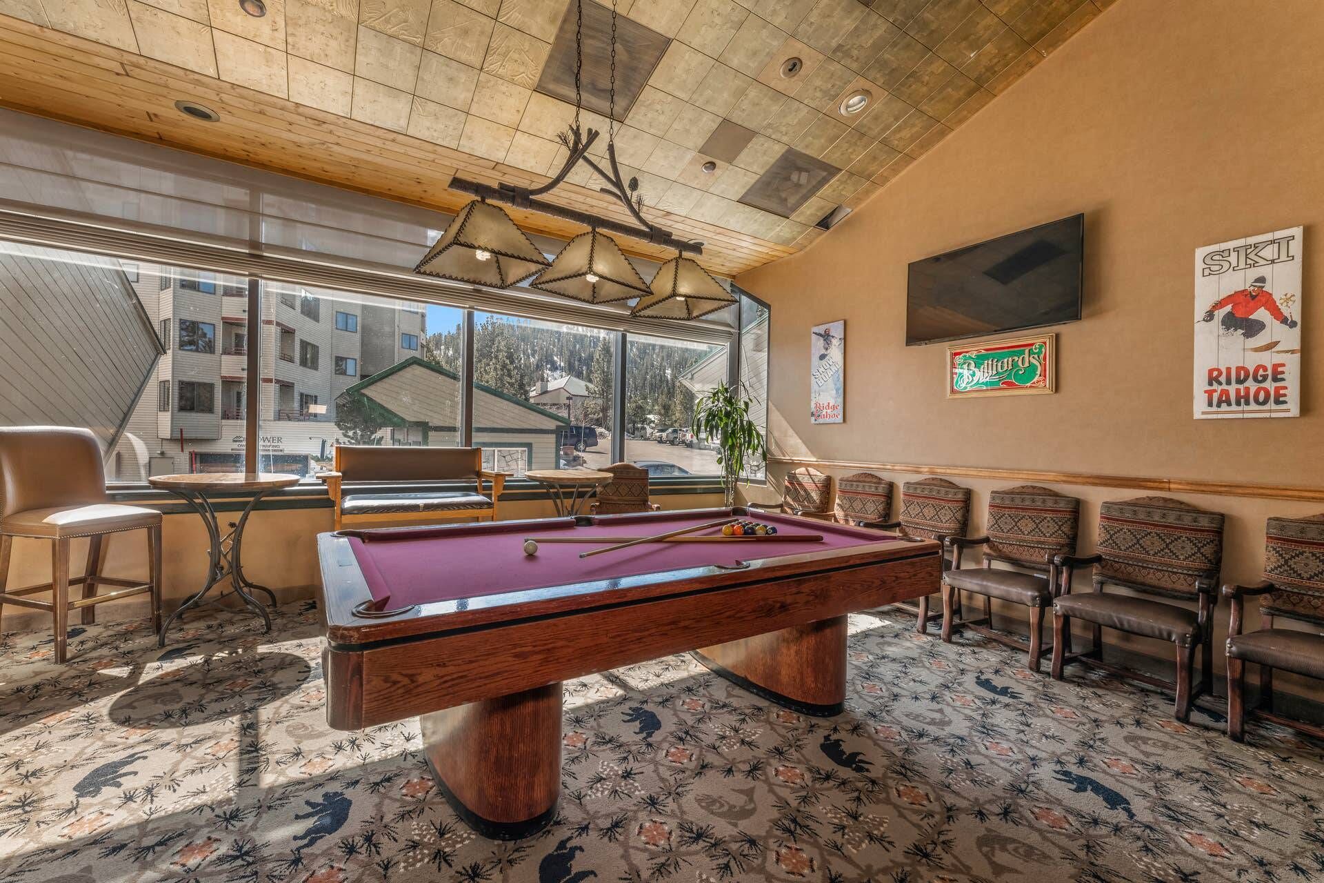 A pool table in a room with a large window, a billiards sign, and a television on the wall.