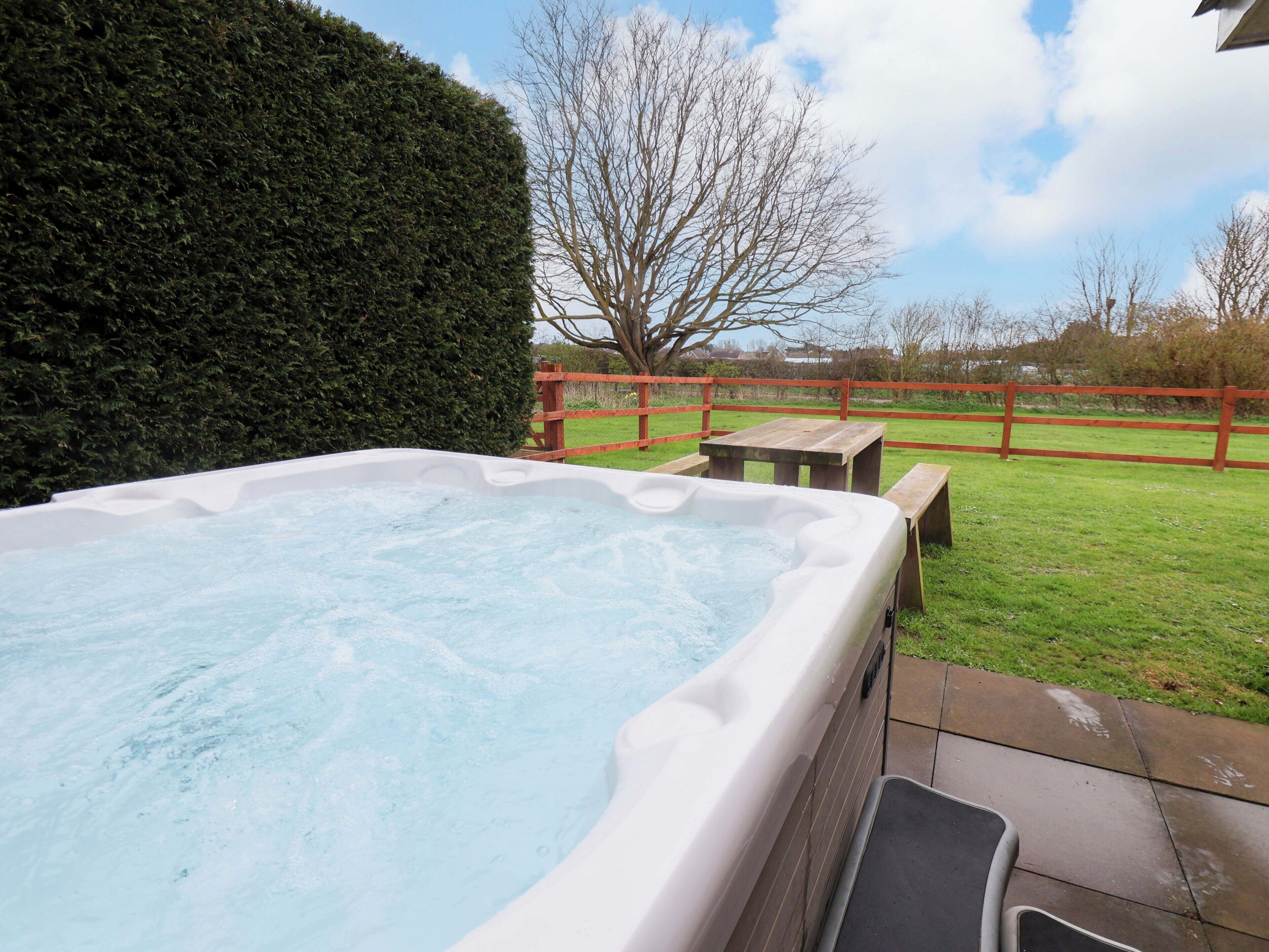 A hot tub in a backyard with a wooden fence, a bench, and a hedge.