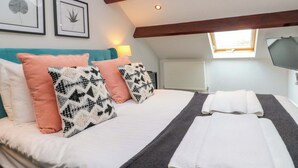 A bedroom with a bed, pillows, a blanket, a TV, a window, and framed leaf art on the wall. - Kittiwake (Bridlington)