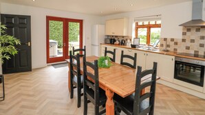 A modern kitchen with a wooden dining table, black chairs, and a built-in oven. - Kittiwake (Bridlington)
