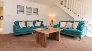 A living room with two teal sofas, a wooden coffee table, a lamp, and a staircase. - Kittiwake (Bridlington)