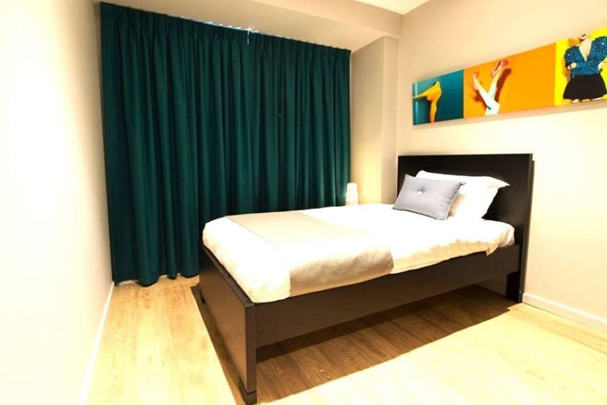 A bedroom with a bed, dark curtains, a painting on the wall, and a wooden floor.