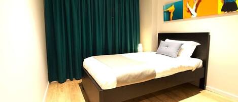Une chambre à coucher avec un lit, des rideaux foncés, un tableau au mur et un plancher en bois.
