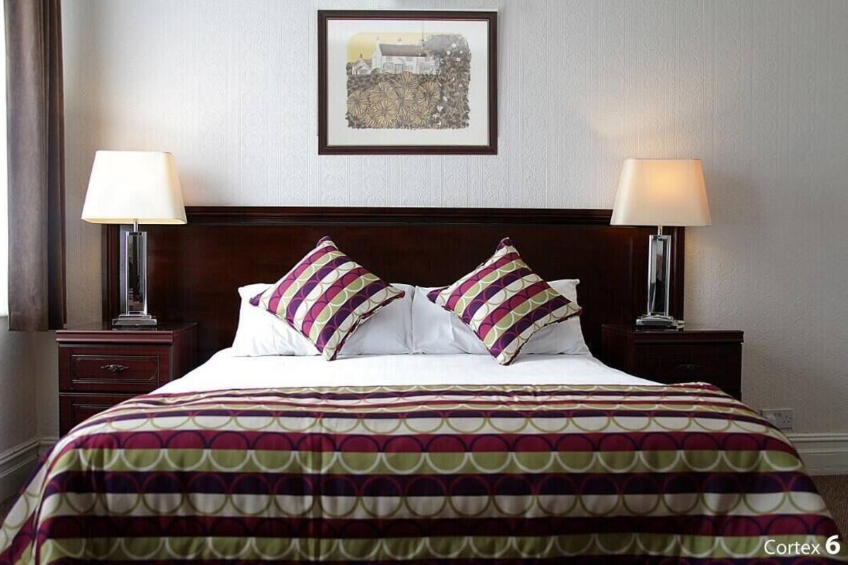 A hotel room with a large bed, two bedside tables with lamps, a framed picture on the wall, and a patterned bedspread.