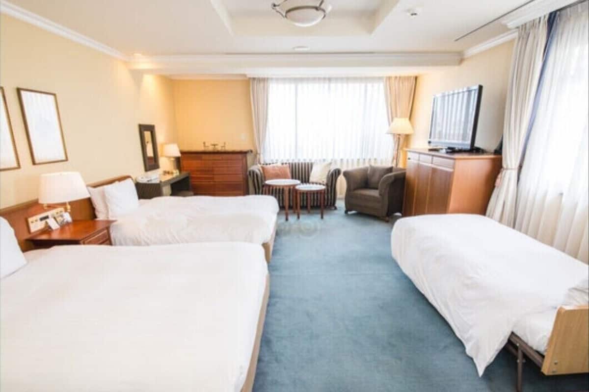 A hotel room with two beds, a TV, a desk with a lamp, a chair, and a small table.