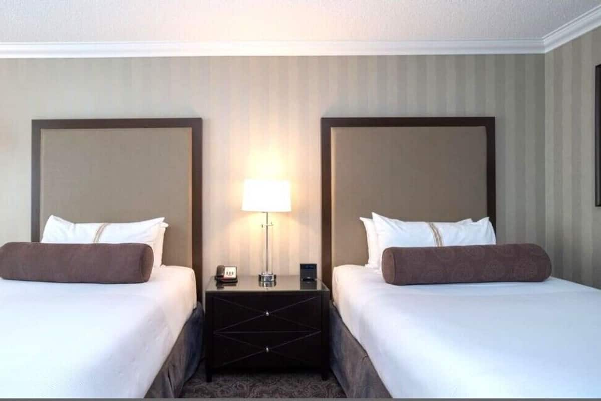 A hotel room with two beds, a nightstand with a lamp, and a wall-mounted clock.