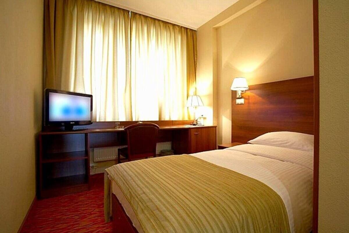 A hotel room with a bed, a desk with a computer, a television, and a lamp.