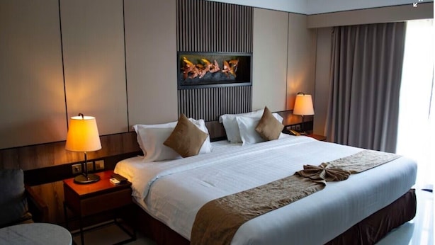 Une chambre d’hôtel avec un grand lit, deux tables de chevet avec des lampes, une petite table ronde et une œuvre d’art accrochée au mur.