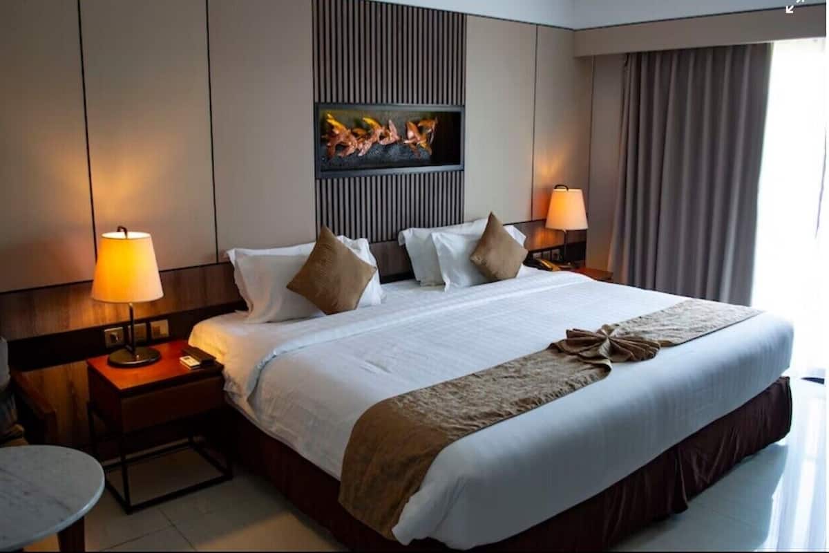 A hotel room with a large bed, two bedside tables with lamps, a small round table, and a wall-mounted artwork.