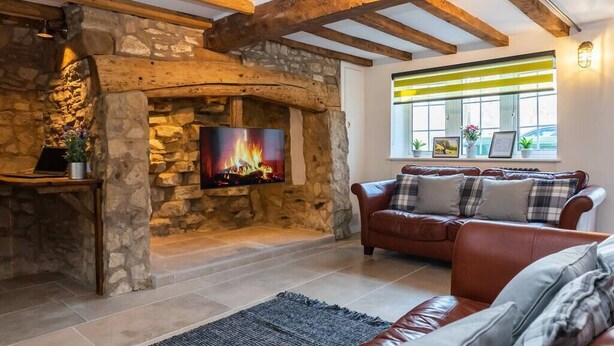 A cozy living room with a stone fireplace, a leather sofa, and a flat-screen TV. - 1 Pound Cottage-4 Bed Home-Parking (Gloucester)
