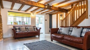 A living room with two brown leather sofas, a grey rug, and a wooden staircase. - 1 Pound Cottage-4 Bed Home-Parking (Gloucester)