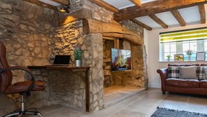 A cozy living room with stone walls, a wooden ceiling, a desk with a laptop, a TV, a leather chair, and a brown leather sofa. - 1 Pound Cottage-4 Bed Home-Parking (Gloucester)