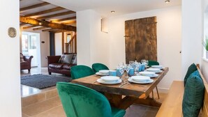 A dining area with a wooden table set for six, green upholstered chairs, and a rustic wooden wall. - 1 Pound Cottage-4 Bed Home-Parking (Gloucester)