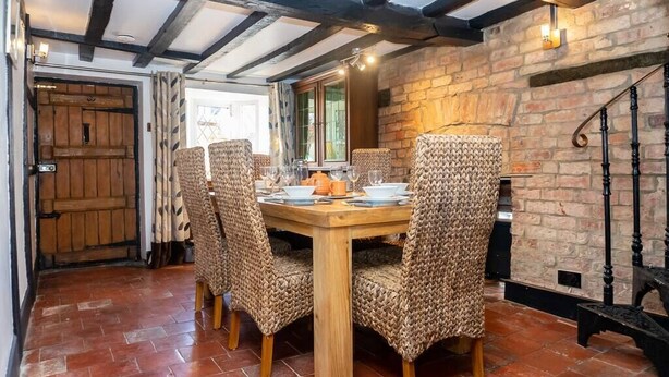 Un espace repas avec une table en bois et des chaises en osier, un mur en pierre et un escalier.