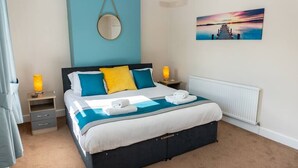 Een net opgemaakt bed met een blauw-witte streepdeken, twee kussens en een bedlampje aan elke kant.