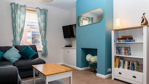 Een woonkamer met een grijze bank, een houten salontafel, een witte boekenkast en een televisie op een dressoir.