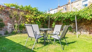 Een terras met vier metalen stoelen en een kleine ronde tafel, omgeven door een bakstenen muur en beplanting.