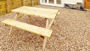 A two-story house with a patio area featuring a wooden table and benches.
