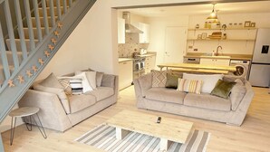 A modern living room with two sofas, a coffee table, and a staircase with gingerbread decorations.