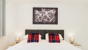 Ein ordentlich bezogenes Bett mit weißer Bettwäsche und einer roten Decke, flankiert von zwei Nachttischen mit Lampen, und ein Wandbild mit zwei Tigern.