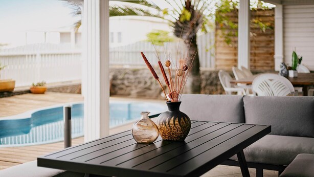 A patio area with a table, chairs, and a vase with decorative items. - T3 Pisicine Chauffée et Privative (Saint-Leu)