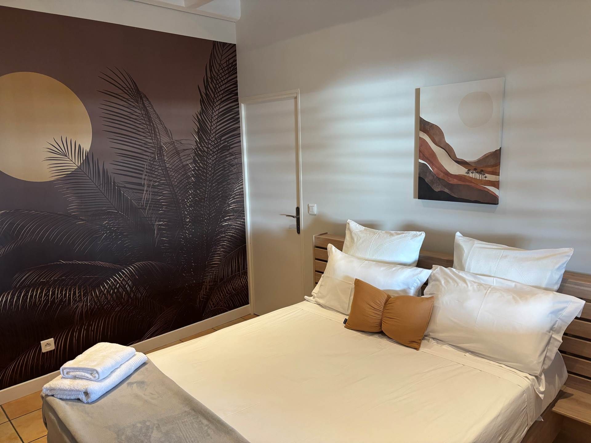 A bedroom with a bed, pillows, a wall mural, and a door.